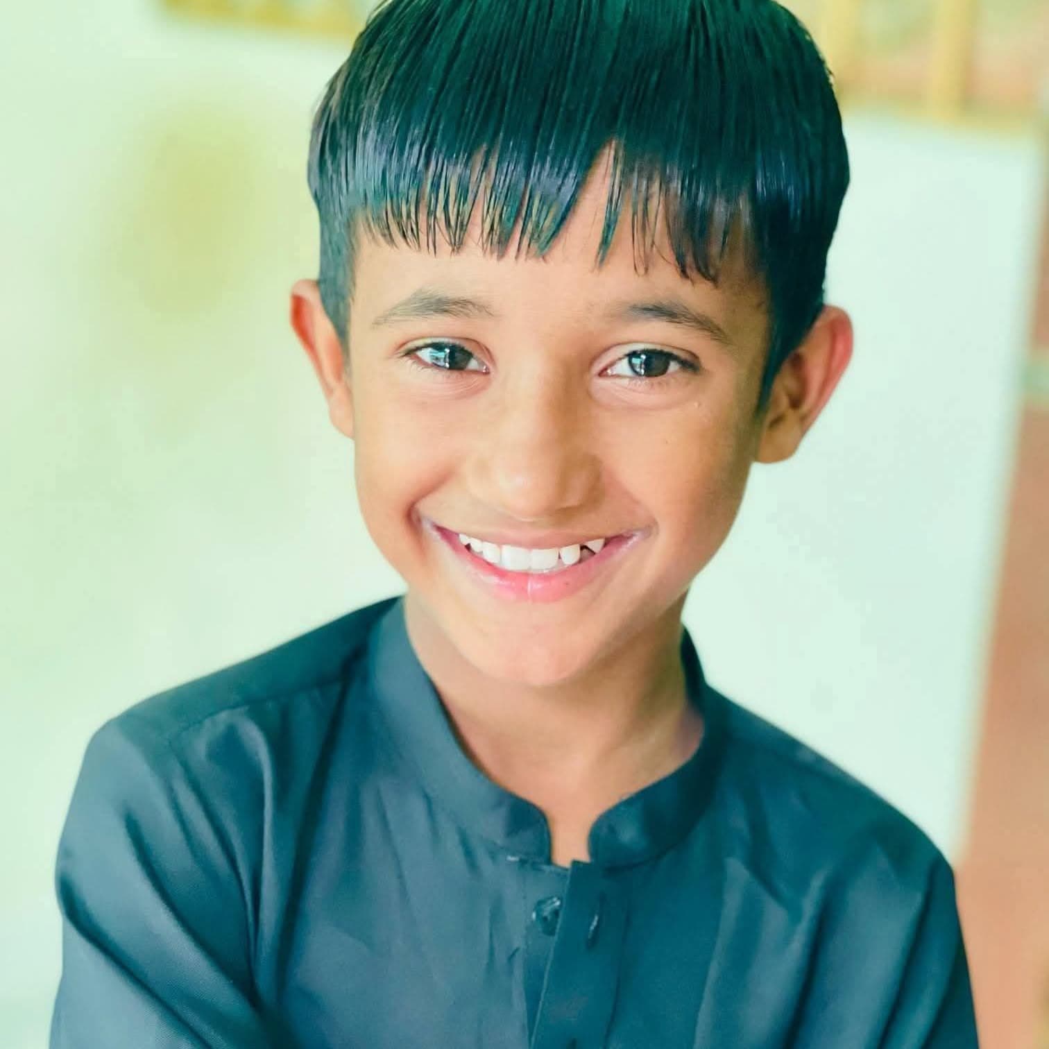 A boy in a dark green kurta, smiling, photographed by the foundation.