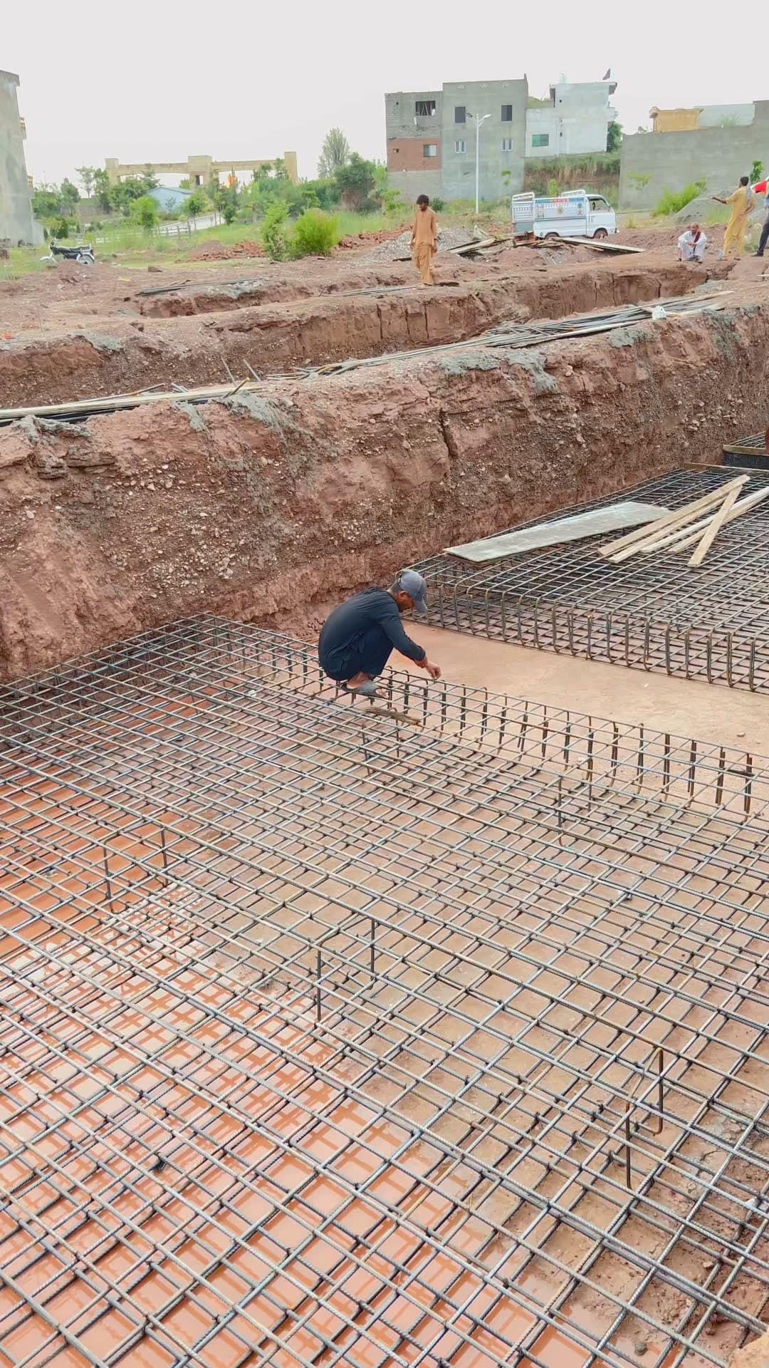 A worker tying steel reinforcement across the poured foundation slab at Parsa Home.